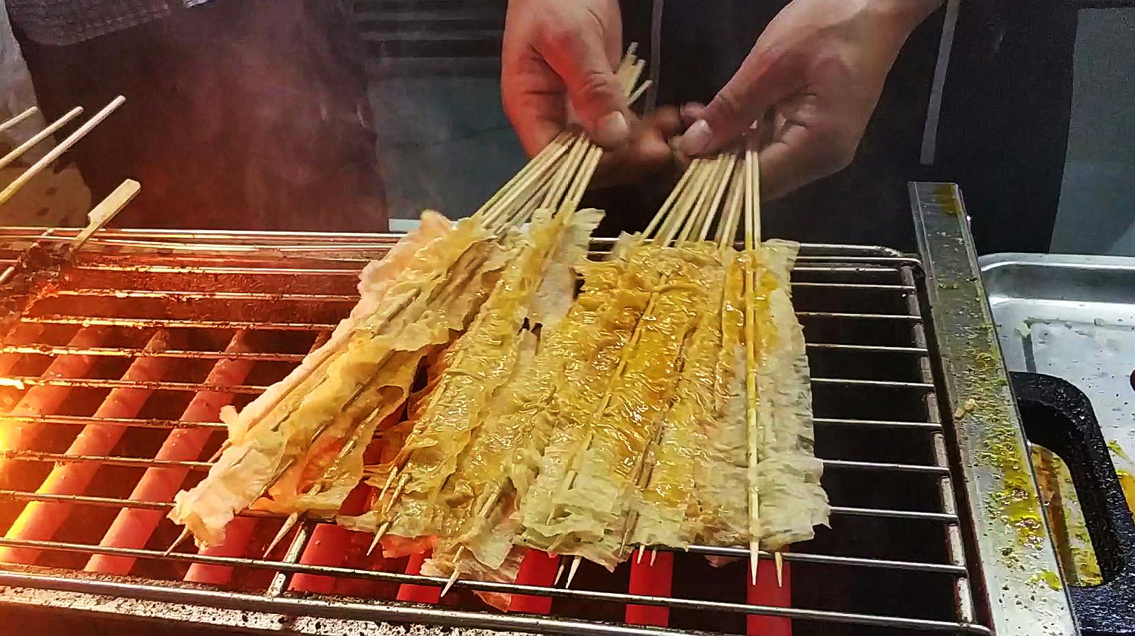 大哥在天津夜市卖烤豆皮,10元一把25串,生意火爆被顾客围着买